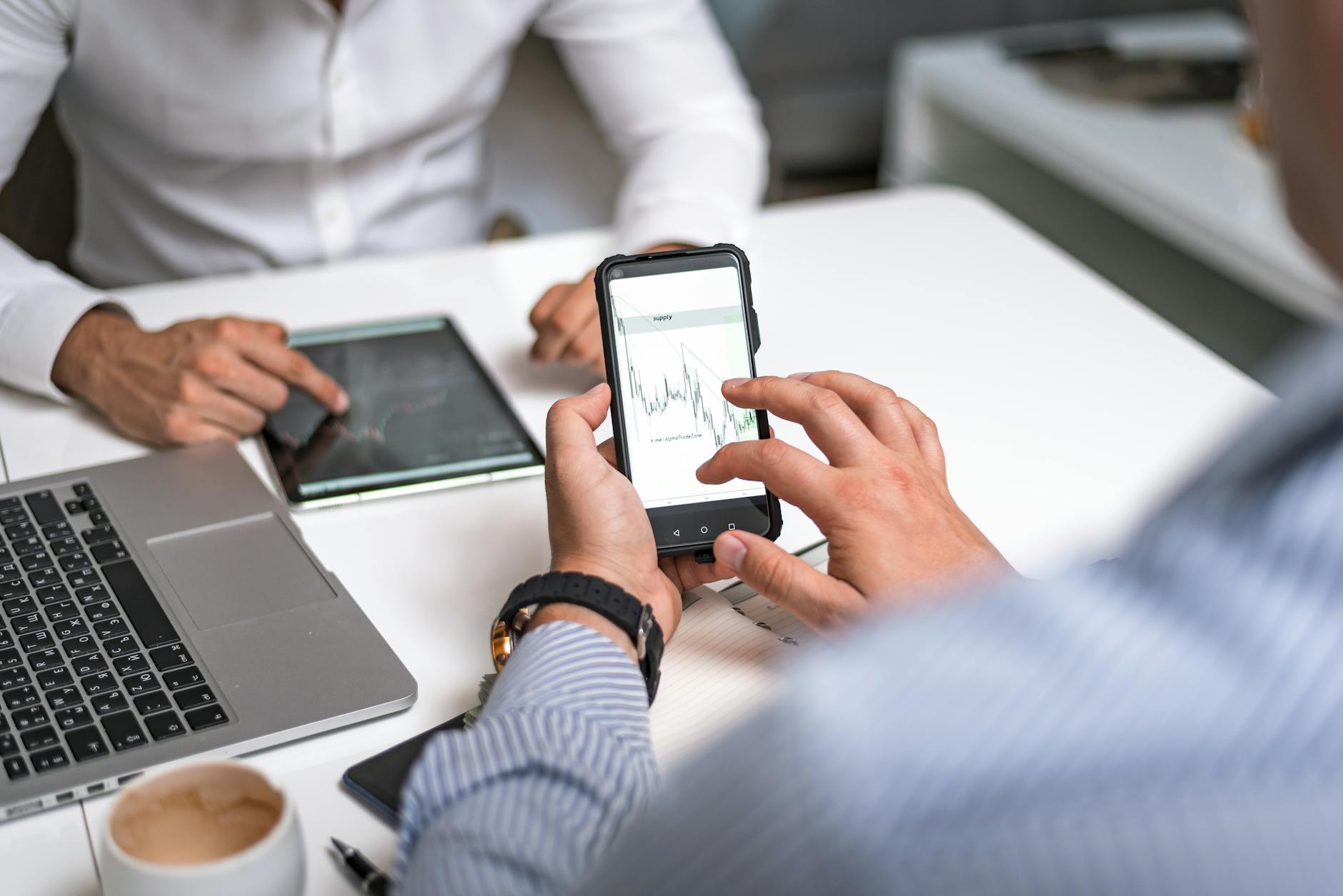 Person holding smartphone showing dual camera view in professional workspace environment